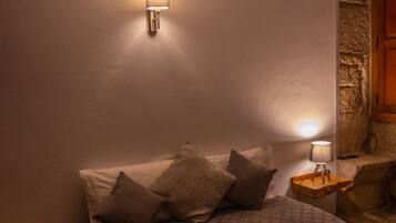 A bedroom with a bed, pillows, a nightstand, a wall-mounted lamp, and a stone accent wall.