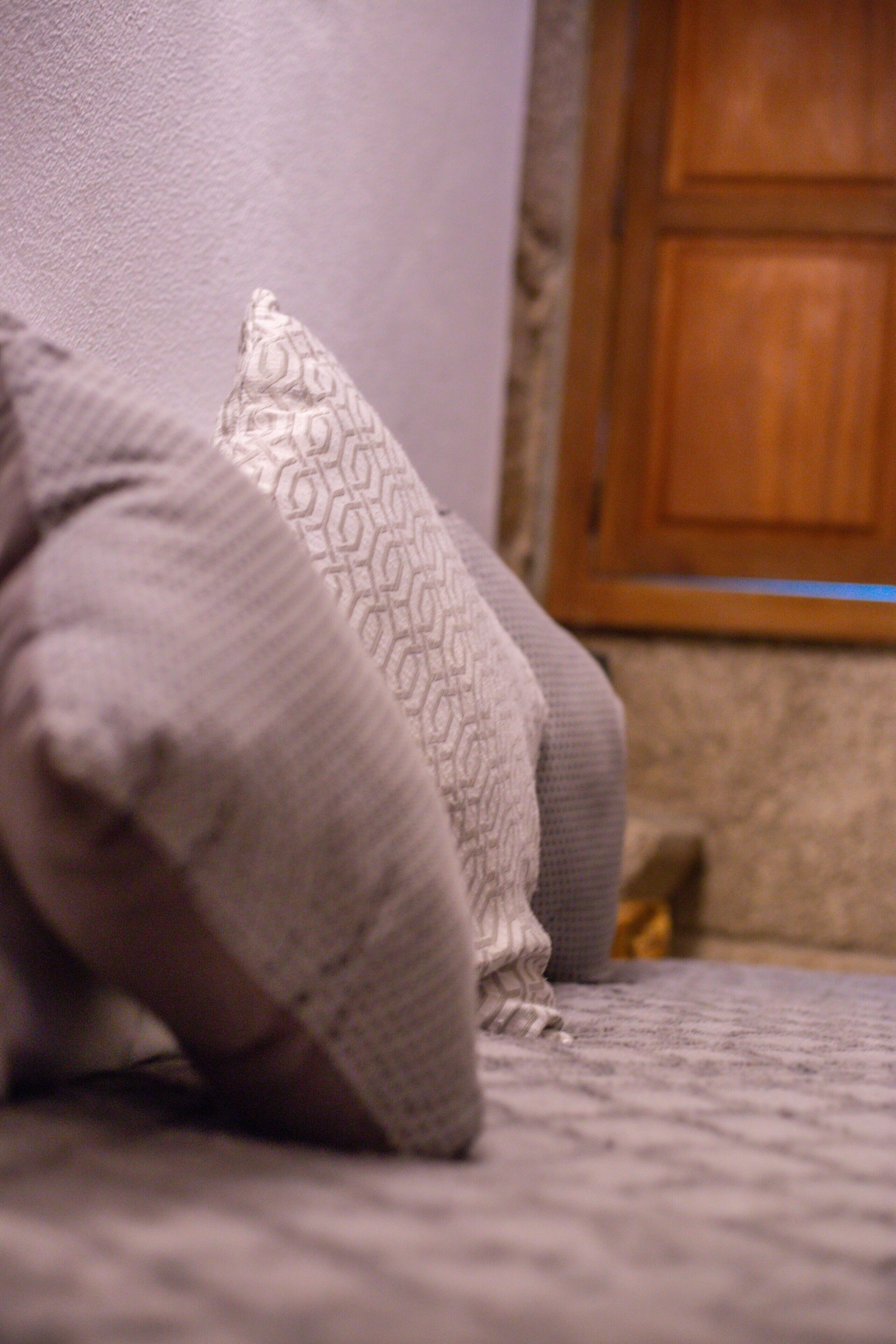 A bed with pillows and a blanket, a wooden door in the background, and a carpeted floor.