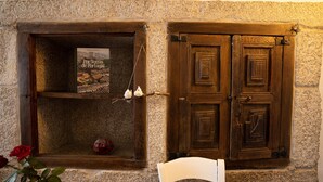 Paredes de pedra com uma porta de madeira e um livro intitulado 'Por Terras de Portugal' numa estante.