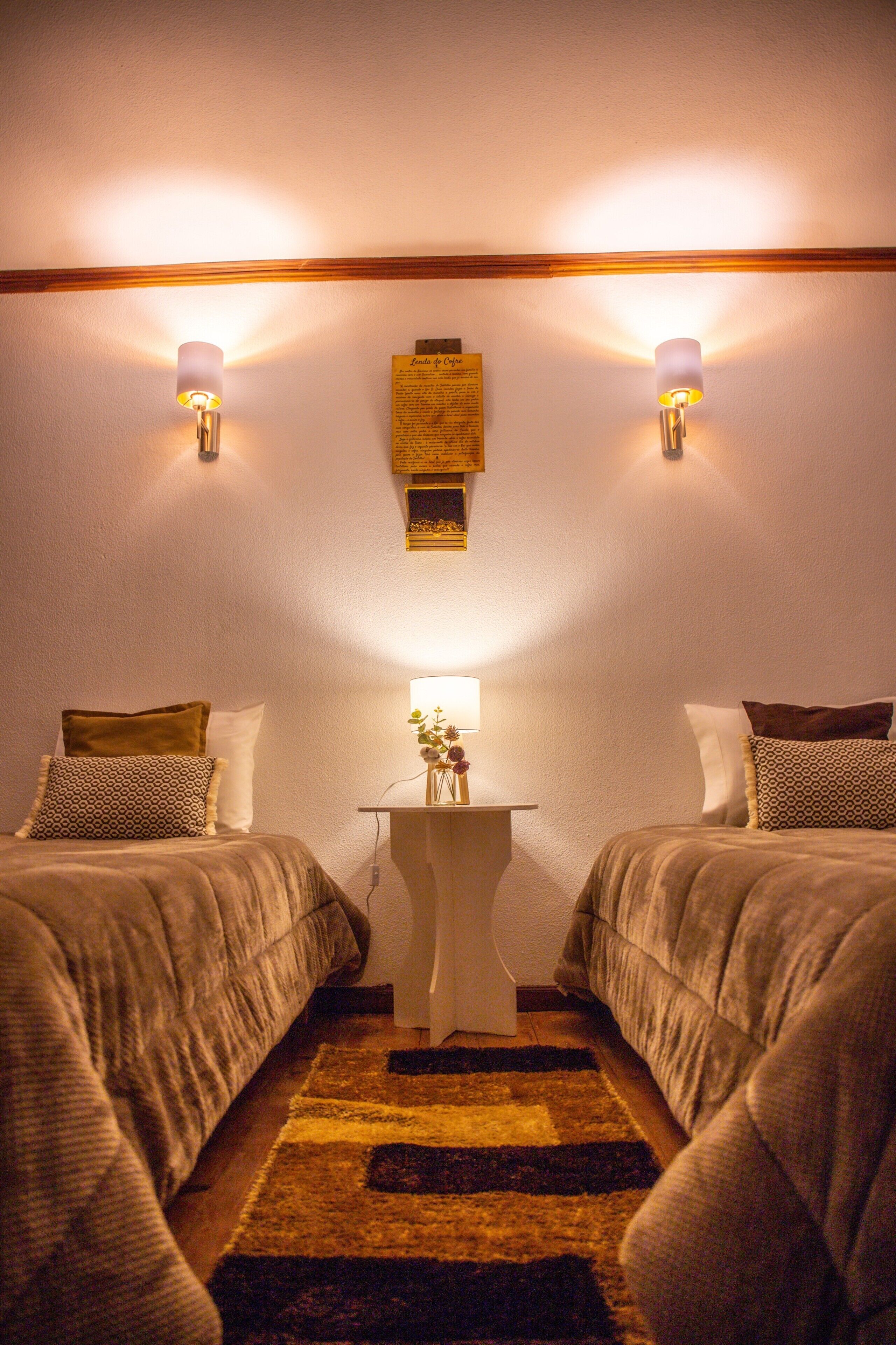 Une chambre avec deux lits, une petite table avec une lampe et deux lampes fixées au mur.