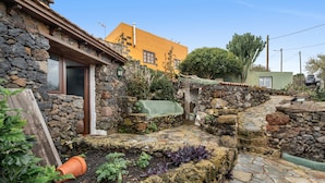 Une cour entourée de murs en pierre, avec une petite maison, un cactus et une voiture garée à l’extérieur.