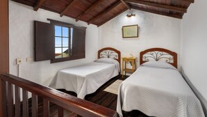 Une chambre avec deux lits, des poutres apparentes en bois au plafond, une fenêtre et une petite table de chevet.