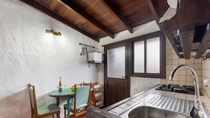Une cuisine équipée d’un évier, de poutres en bois au plafond, d’une petite table avec des chaises et d’un micro-ondes posé sur une étagère.