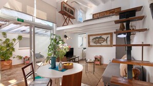 Una habitación amplia con una mesa de comedor, sillas, un sofá, un televisor y una escalera que sube a un nivel superior.