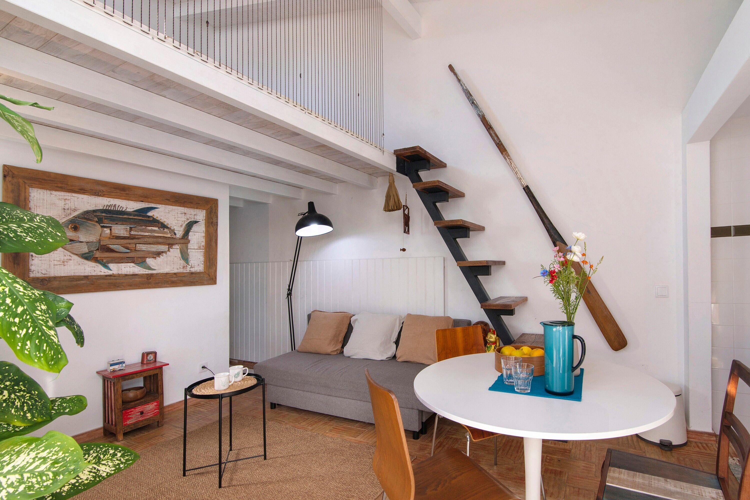 Un interior moderno con un sofá, una mesa de comedor, sillas, una escalera y una planta grande.