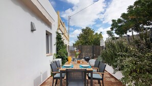 A patio with a table set for four, surrounded by chairs, and a white building in the background. - Holiday Home 'Casa Do Limoeiro' with Private Garden, Wi-Fi and Air Conditioning (Cacela Velha)