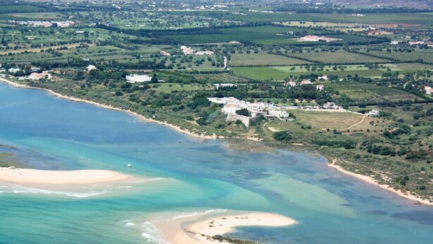An aerial view of a coastal area with a beach, clear waters, and scattered buildings. - Holiday Home 'Casa Do Limoeiro' with Private Garden, Wi-Fi and Air Conditioning (Cacela Velha)