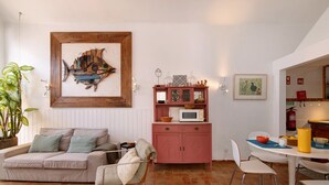 A cozy living area with a sofa, a chair, a dining table with chairs, a pink cabinet, and a framed artwork on the wall. - Holiday Home 'Casa Do Limoeiro' with Private Garden, Wi-Fi and Air Conditioning (Cacela Velha)
