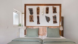 A bedroom with a wooden headboard, two green pillows, a bed with a patterned bedspread, and a wall-mounted clock. - Holiday Home 'Casa Do Limoeiro' with Private Garden, Wi-Fi and Air Conditioning (Cacela Velha)