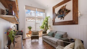 A living room with a sofa, armchair, wooden shelves, a potted plant, and a painting on the wall. - Holiday Home 'Casa Do Limoeiro' with Private Garden, Wi-Fi and Air Conditioning (Cacela Velha)