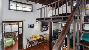 A rustic kitchen with a wooden staircase, a dining area with chairs, and a stone wall. - Apartment 'Tesbabo Rural - Mimo' with Sea View, Shared Garden and Wi-Fi (Mocanal)