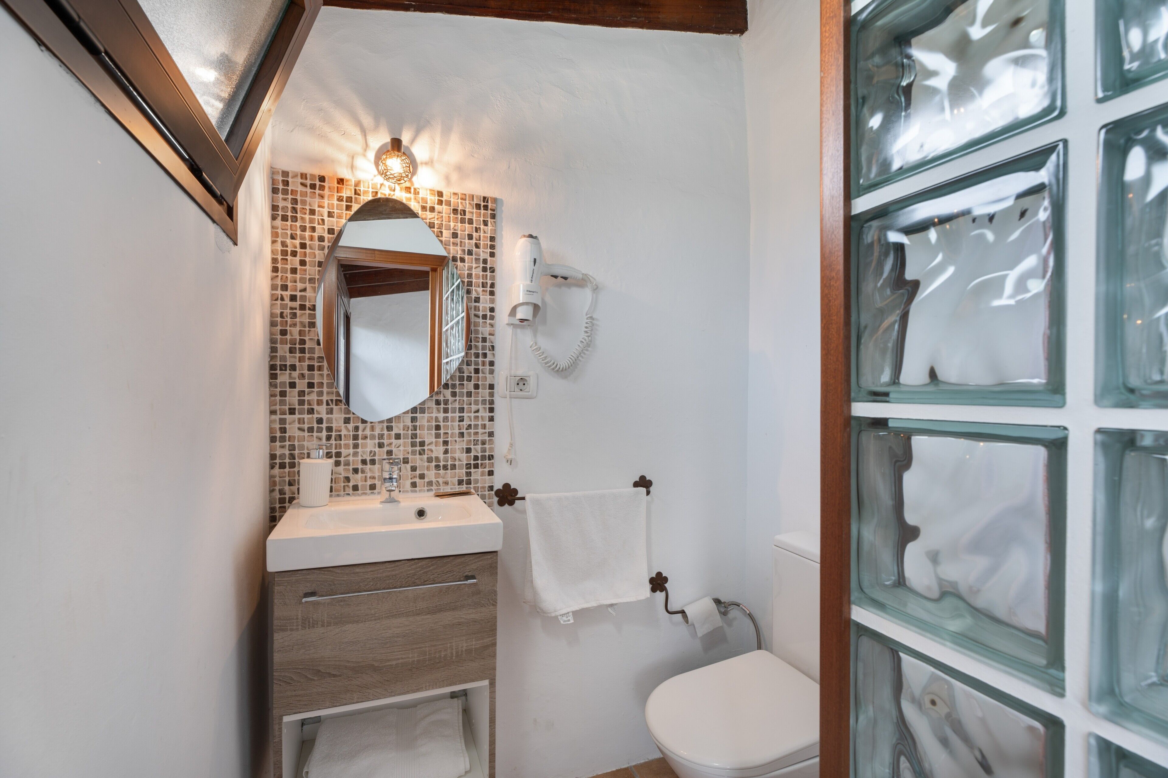 A bathroom with a tiled backsplash, a sink, a mirror, a towel rack, and a toilet.