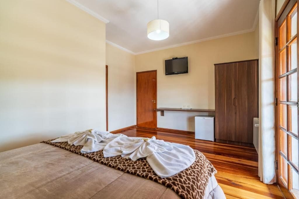 Um quarto com uma cama, televisão na parede, guarda-roupa e janela com cortinas.