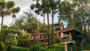 A multi-story building with a red facade, surrounded by lush greenery and tall trees. - Serra do Jordão by Concavus (Campos do Jordão)