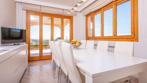 A modern kitchen with a dining area, large windows, and a television.