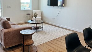 A modern living room with a sofa, two round tables, a TV mounted on the wall, and a ceiling fan. - “Freiheit Loft” Lush Couple’s Getaway by Gruene (New Braunfels)