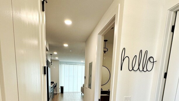 A hallway with wooden flooring, white walls, and a 'hello' sign on one door. - “Freiheit Loft” Lush Couple’s Getaway by Gruene (New Braunfels)