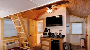 Een compacte slaapkamer met een slaapgedeelte op entresol, houten plafond, plafondventilator, flatscreen-tv, kitchenette met magnetron, koffiezetapparaat en kleine koelkast.
