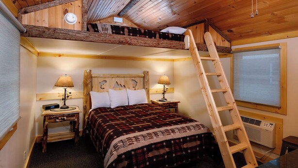 Een knus slaapkamer met een hoogslaper, houten wanden, een ladder en een raam met zonwering.