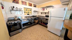 A kitchen with a stove, sink, and refrigerator. There are shelves above the sink and a microwave to the right.