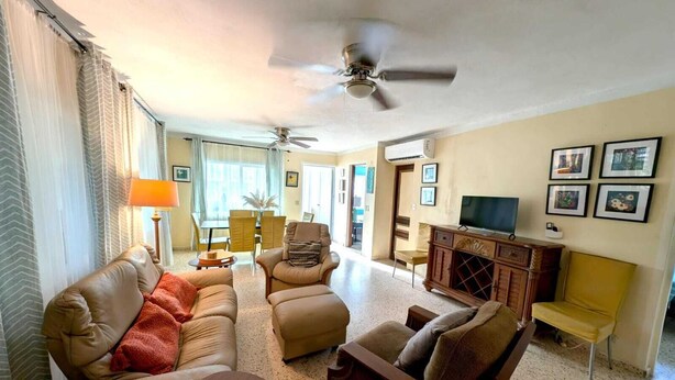 A living room with a sofa, armchairs, a coffee table, a TV, and a ceiling fan.