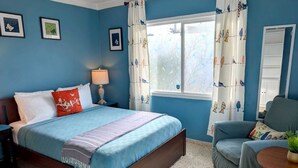 A bedroom with a bed, a chair, a lamp, and a window with curtains.