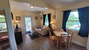 A cozy living room with a sofa, a dining table with chairs, a small coffee table, and a door leading outside. - Sunny 1 bedroom in Esperanza close to everything (Vieques)