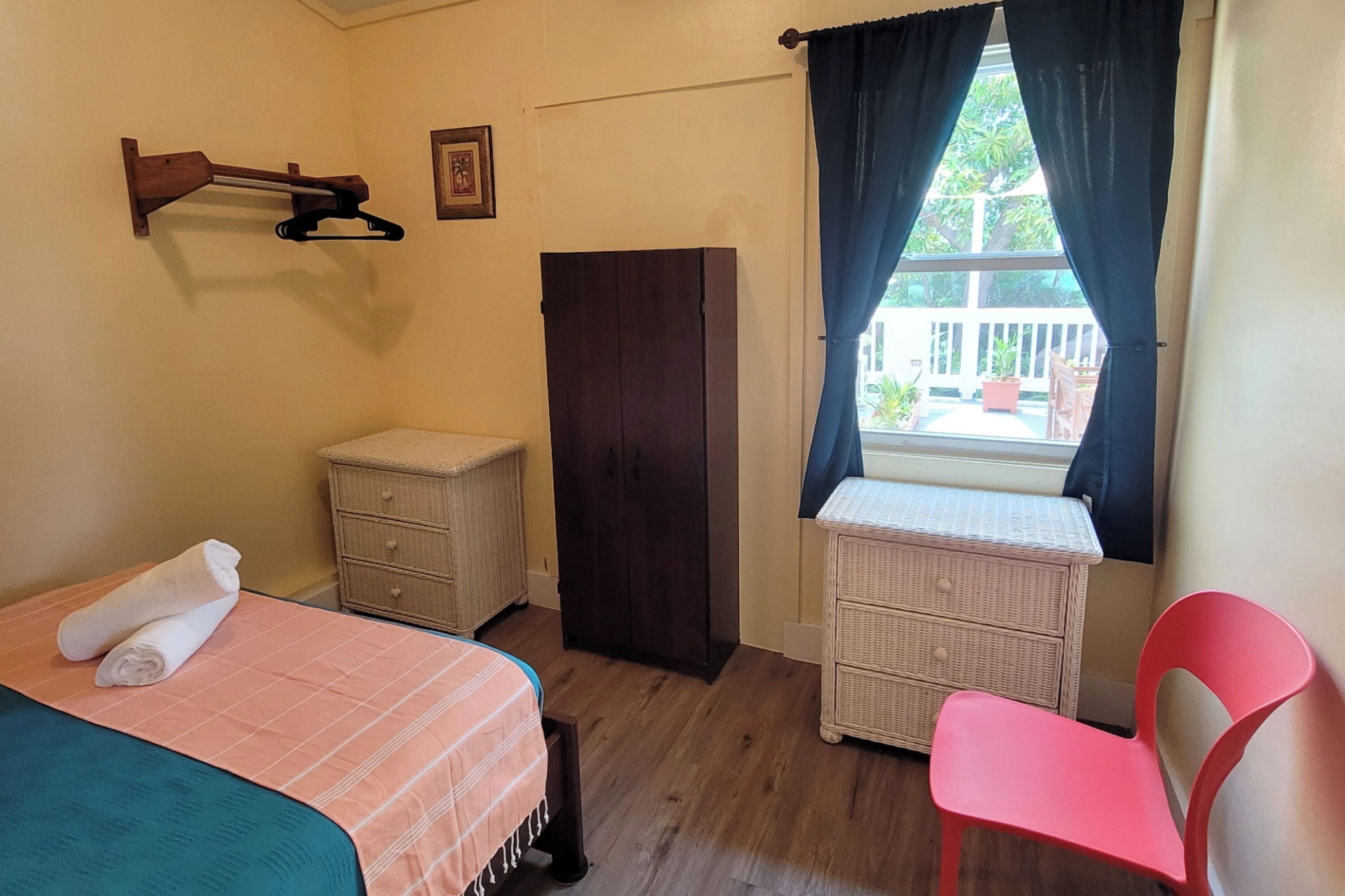 A bedroom with a bed, a wardrobe, a dresser, a chair, and a window with curtains.
