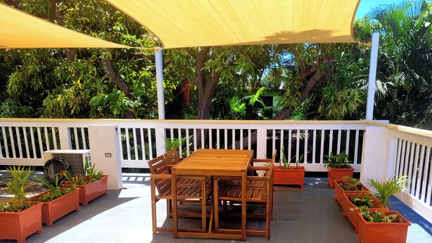 An outdoor patio with a wooden table and chairs, surrounded by potted plants and a white fence. - Sunny 1 bedroom in Esperanza close to everything (Vieques)