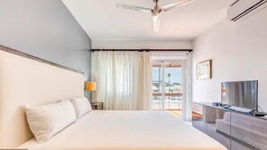 A hotel room with a large bed, a ceiling fan, a TV, and a view of the outdoors. - Stunning 2-BDR apartment with pool/sea view I-403 (BAVARO)