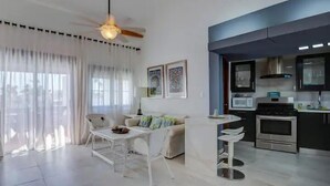 A modern living room with a dining table, sofa, and a ceiling fan. Adjacent is a kitchen with a microwave, stove, and cabinets. - Stunning 2-BDR apartment with pool/sea view I-403 (BAVARO)