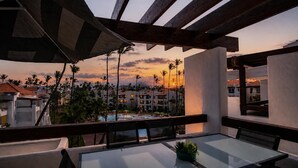 A balcony with a glass table and chairs, overlooking a pool and resort buildings during sunset. - Stunning 2-BDR apartment with pool/sea view I-403 (BAVARO)