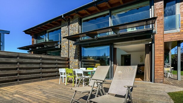 Ett modernt hus med en veranda, utomhusmöbler och stora fönster.