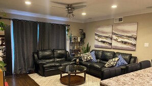 A living room with a black leather sofa, a glass coffee table, and a dining area with a granite countertop. - Charming 3-bedroom cottage in enchanting Citrus Heights with AC, WiFi (Citrus Heights)