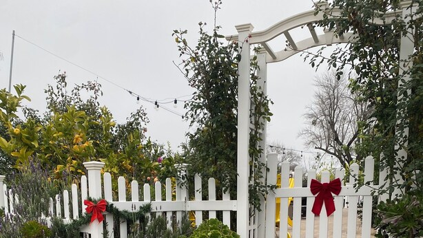 A gated entrance with a white picket fence, red bows, and a brick pathway leading to a covered area. - Charming 3-bedroom cottage in enchanting Citrus Heights with AC, WiFi (Citrus Heights)