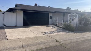 A single-story house with a black garage door, a white picket fence, and a concrete driveway. - Charming 3-bedroom cottage in enchanting Citrus Heights with AC, WiFi (Citrus Heights)
