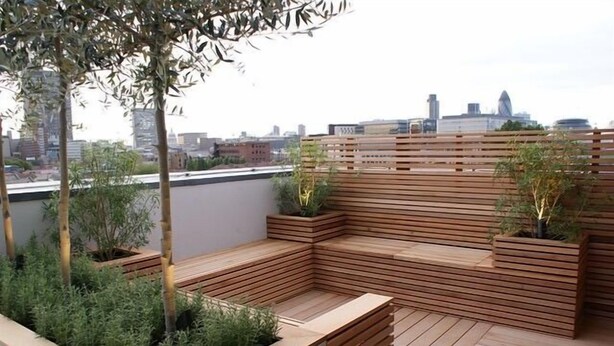 En tagterrasse med træsæder og plantekasser, med udsigt over byens skyline.