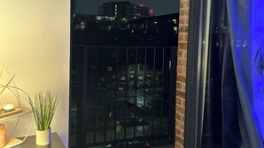En balkon med udsigt over bybilledet om natten, en potteplante og et stearinlys på et bord.