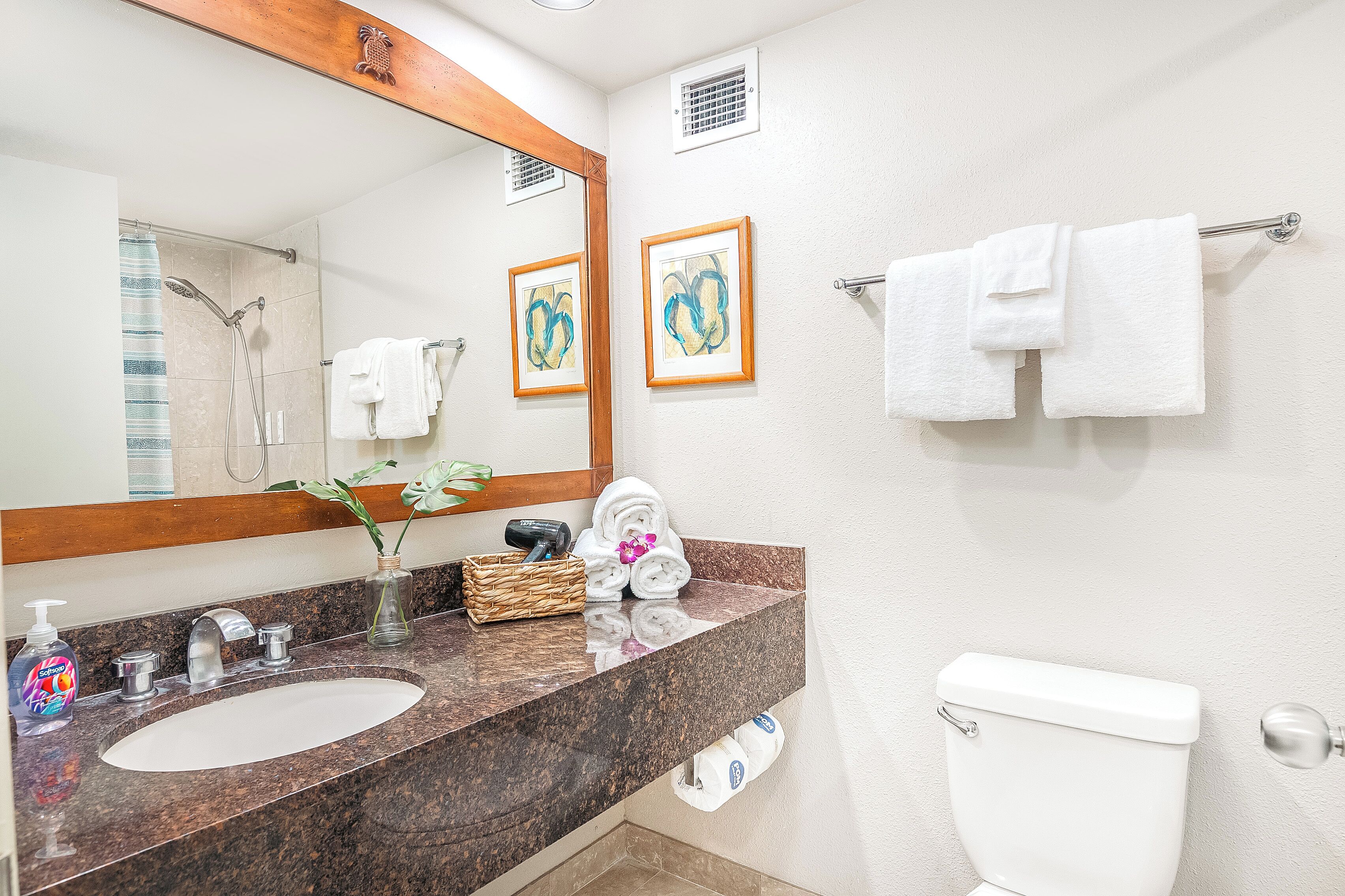 A bathroom with a marble sink, a toilet, a towel rack, and framed artwork on the wall.