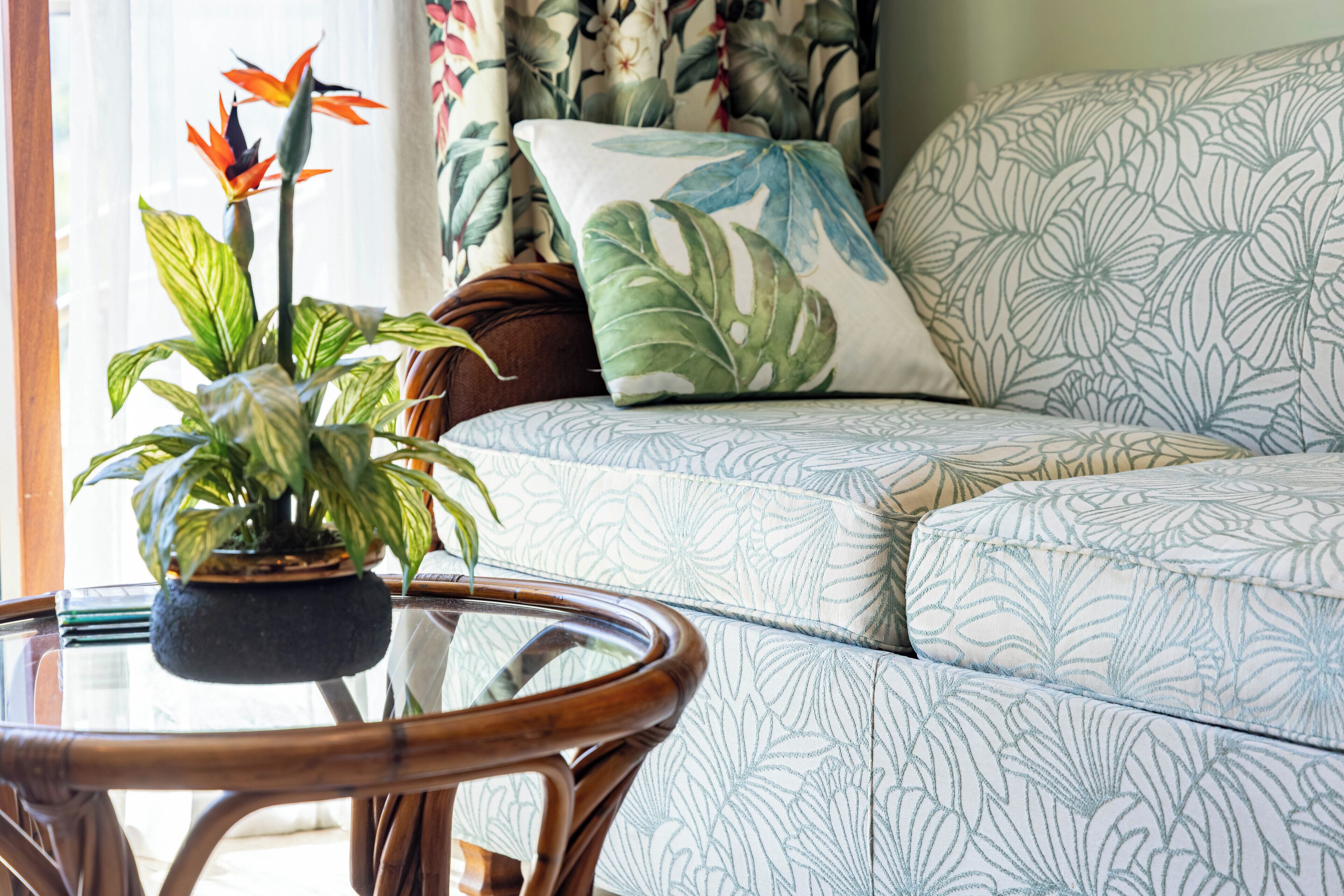 A living room with a patterned sofa, a round glass coffee table, and a potted plant.