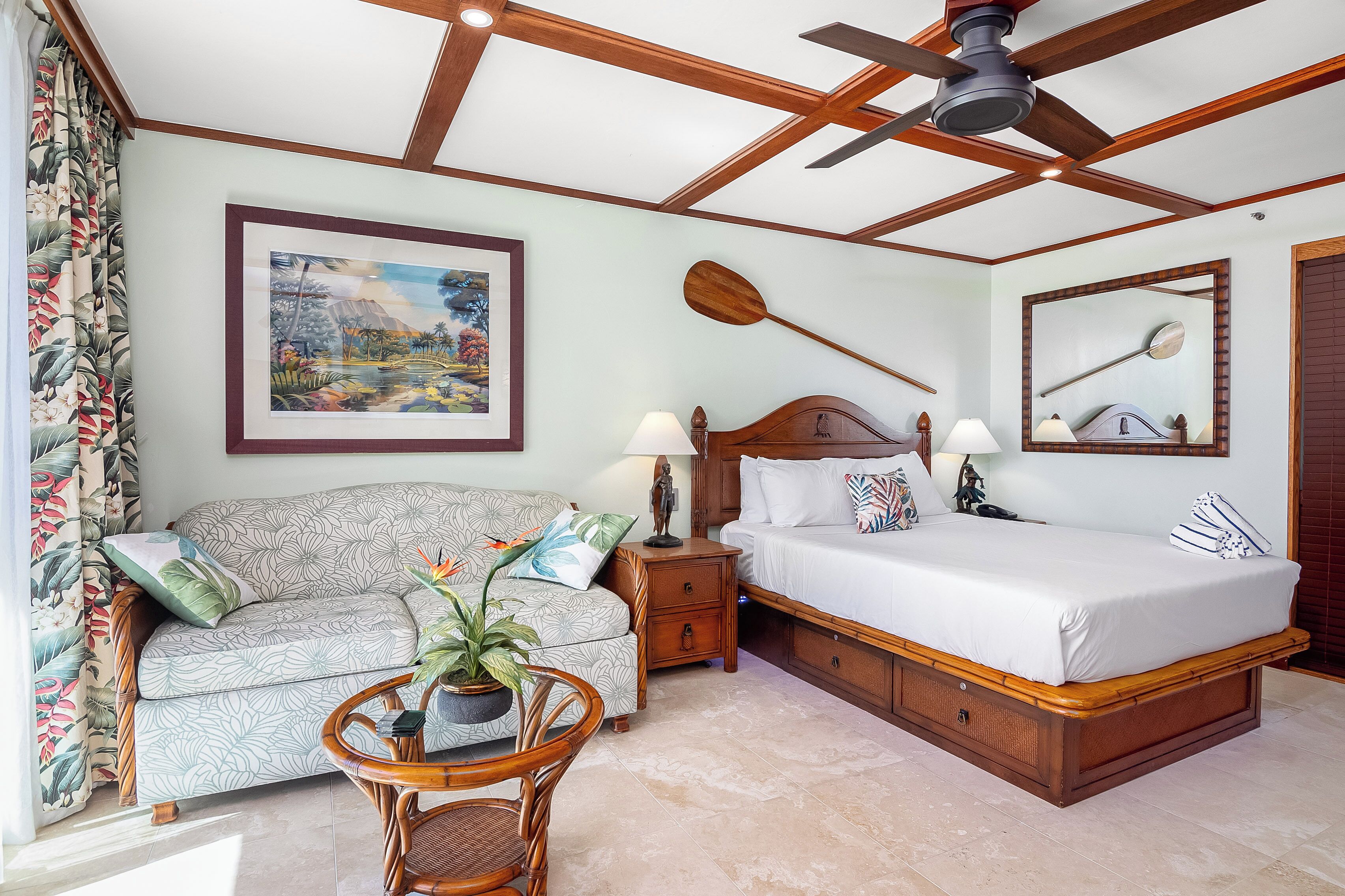 A well-lit bedroom with a bed, a sofa, a nightstand, and a ceiling fan.