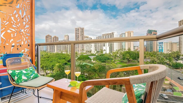 A balcony with wicker chairs, a table, and a city view.