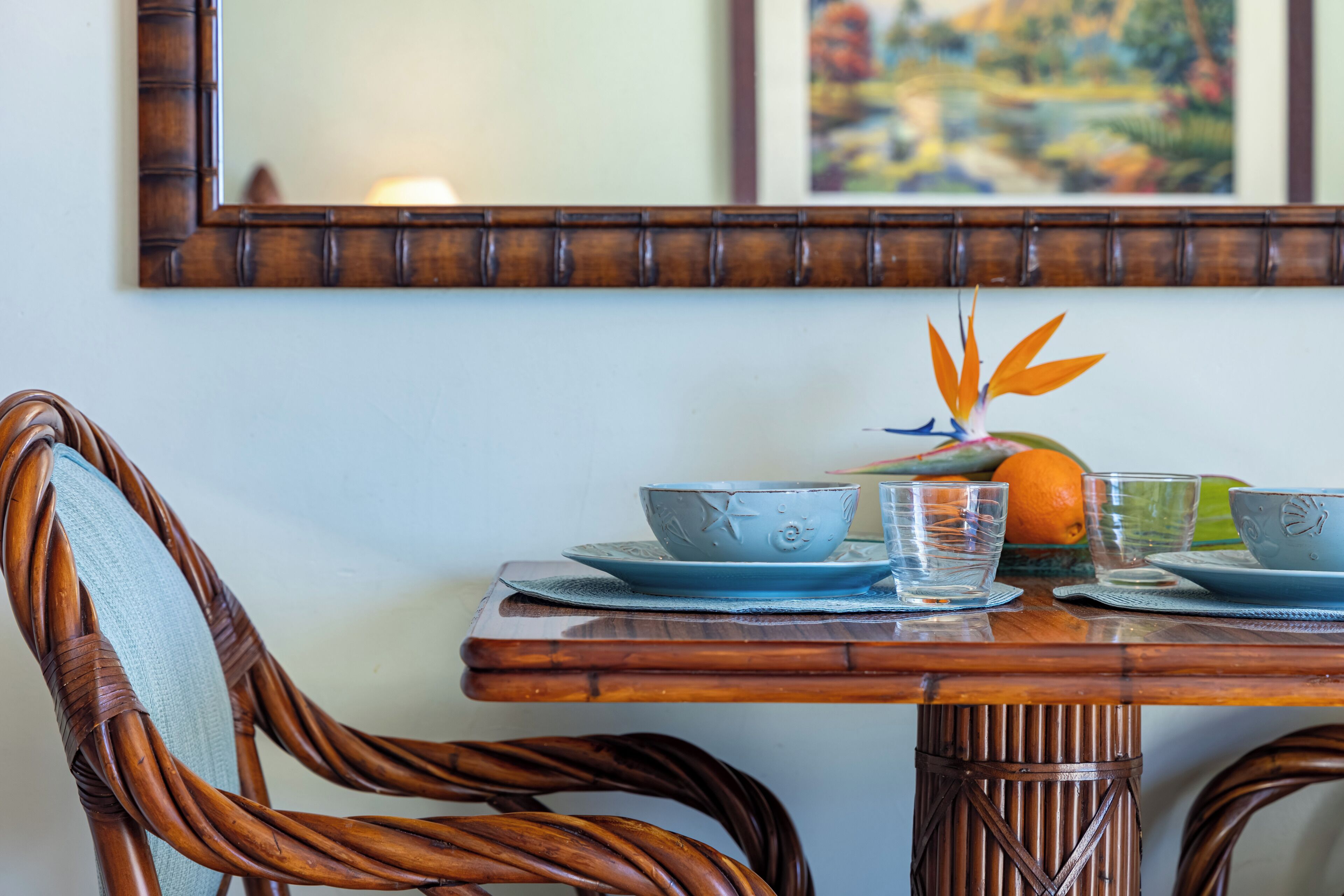 A dining table with blue ceramic bowls and glasses, a woven chair, and a mirror on the wall.