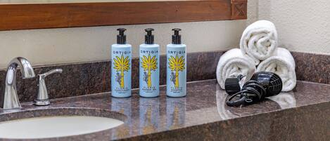 A bathroom counter with three bottles of shower gel, a hairdryer, and a stack of towels.
