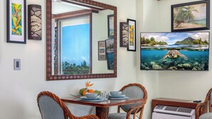 A dining area with a wooden table, wicker chairs, and a mounted flat-screen TV displaying a sea turtle.