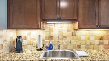 Una cocina con encimeras de granito, pileta de acero inoxidable y muebles de madera.