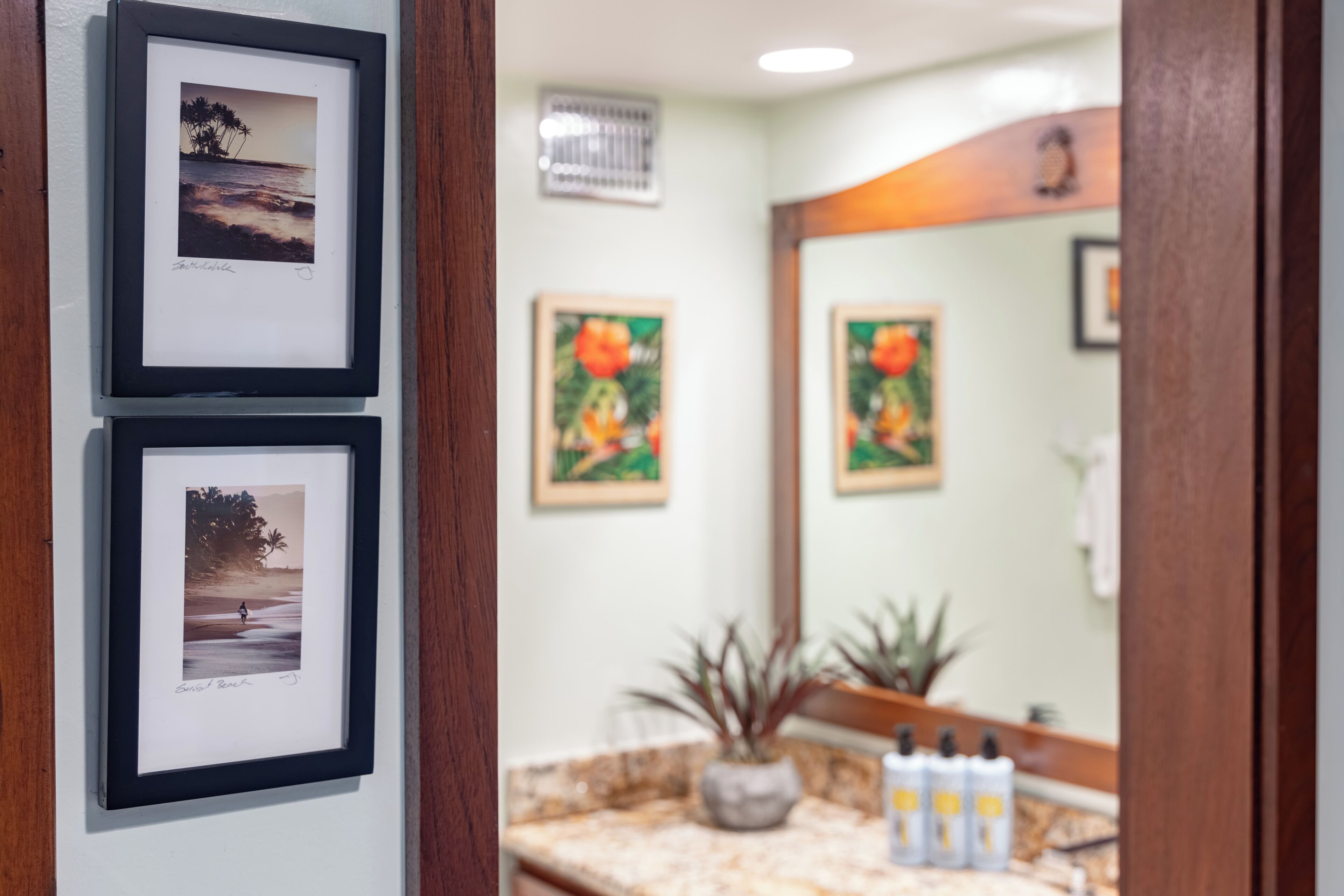 A bathroom with framed photographs on the wall, a sink with toiletries, and a mirror reflecting the room.