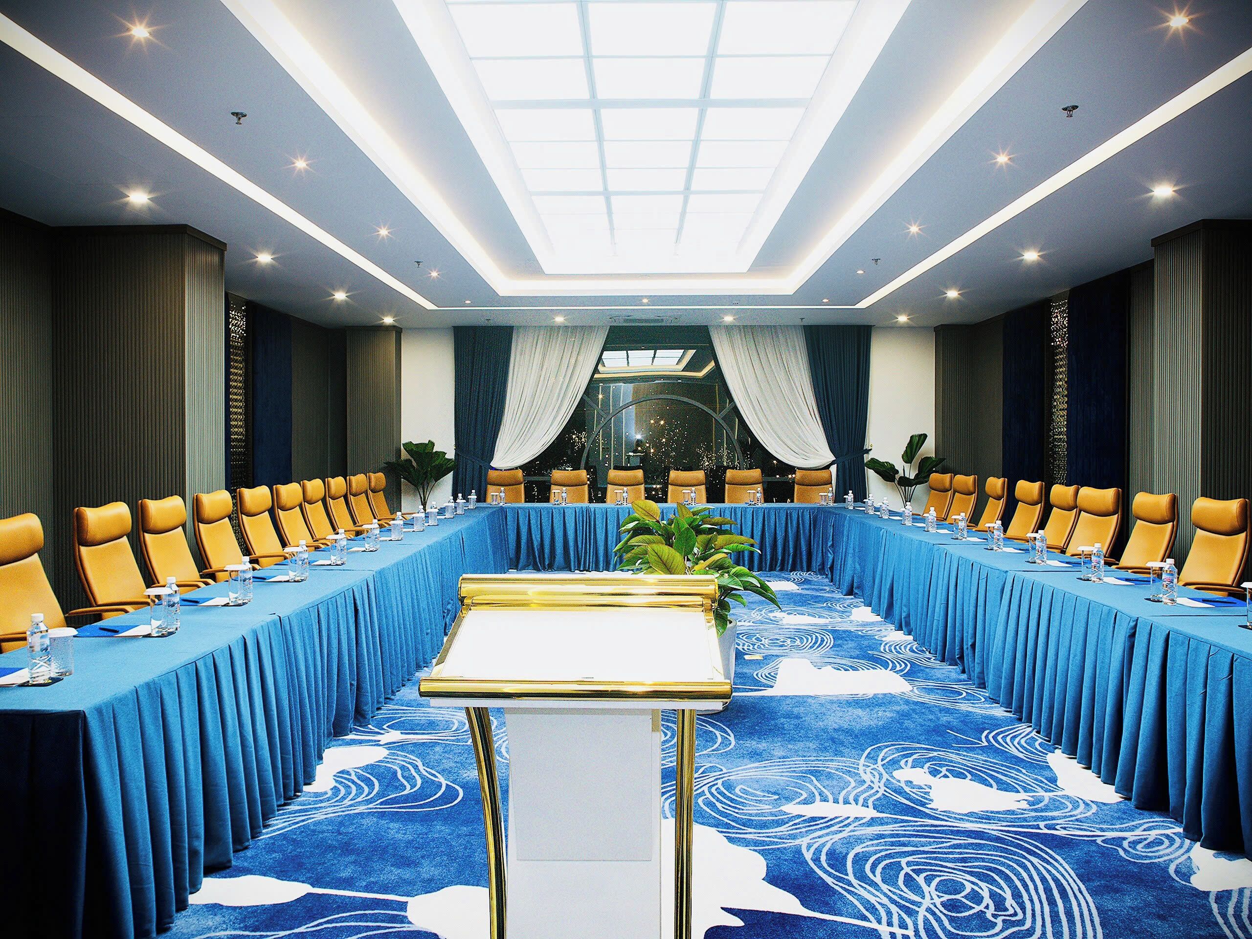 Un salón de conferencias con una larga mesa, varias sillas y un techo con tragaluces.