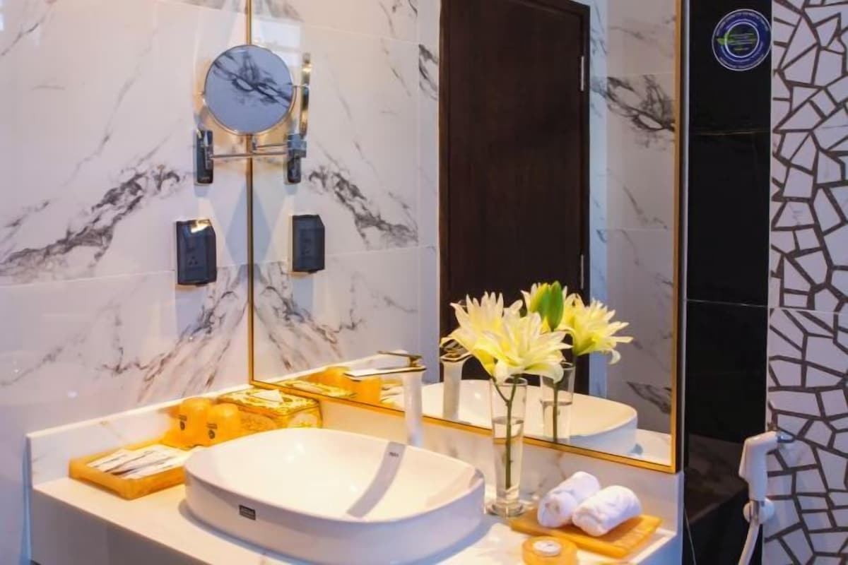 Un baño con un lavabo blanco, un espejo, un perchero y un florero con flores.