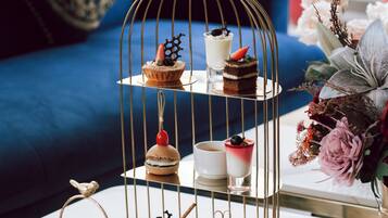 Un soporte de tres niveles para postres con diversos dulces, un arreglo floral y un sofá azul al fondo.